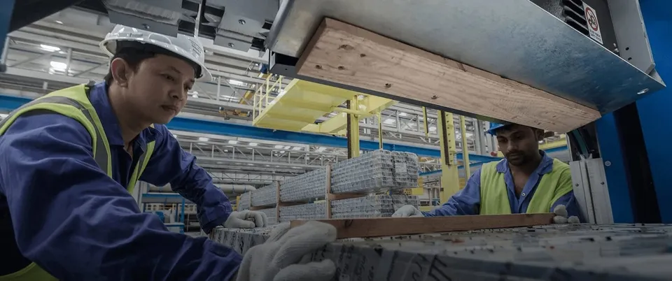 Two Gulf Extrusion operators in hard hats and high-visibility vests guide freshly extruded aluminium profiles along the line.