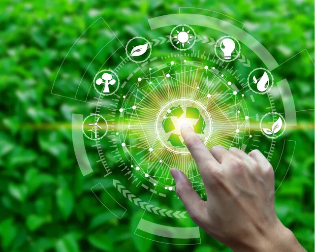 A hand touching a glowing recycling symbol surrounded by renewable-energy icons, over green leaves.