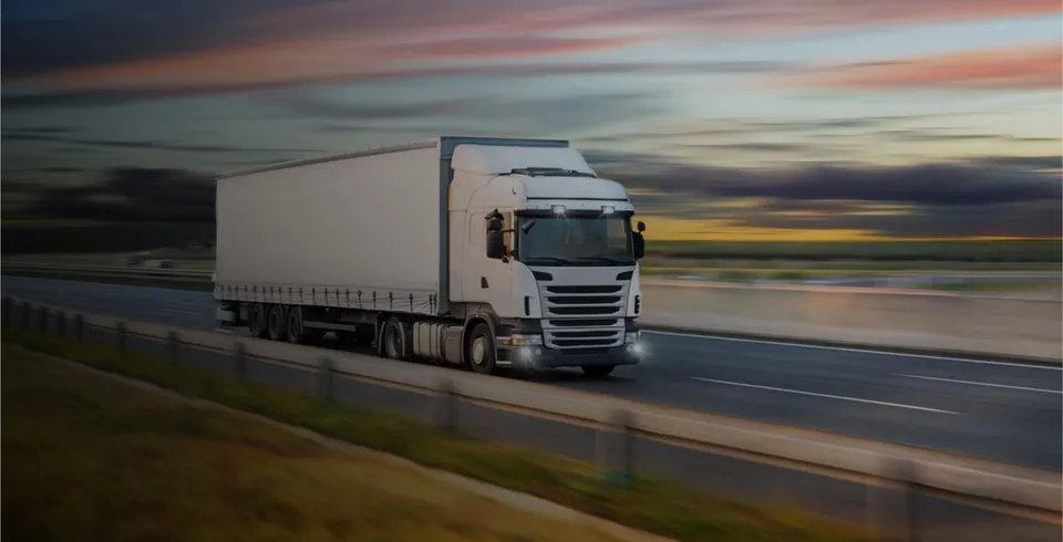 A white articulated lorry with a box trailer driving along a motorway at sunset.